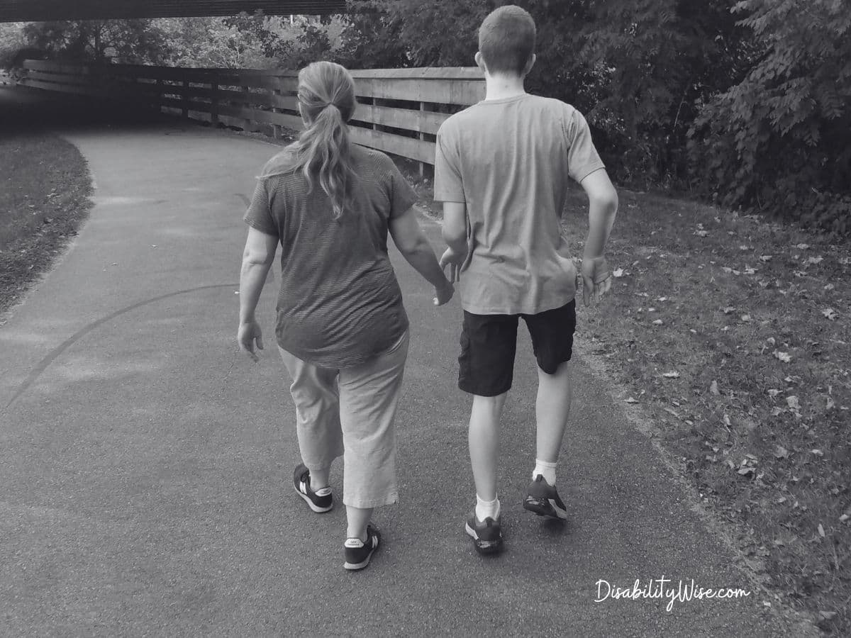 mom and teen son with developmental disabilities walking down a bike path