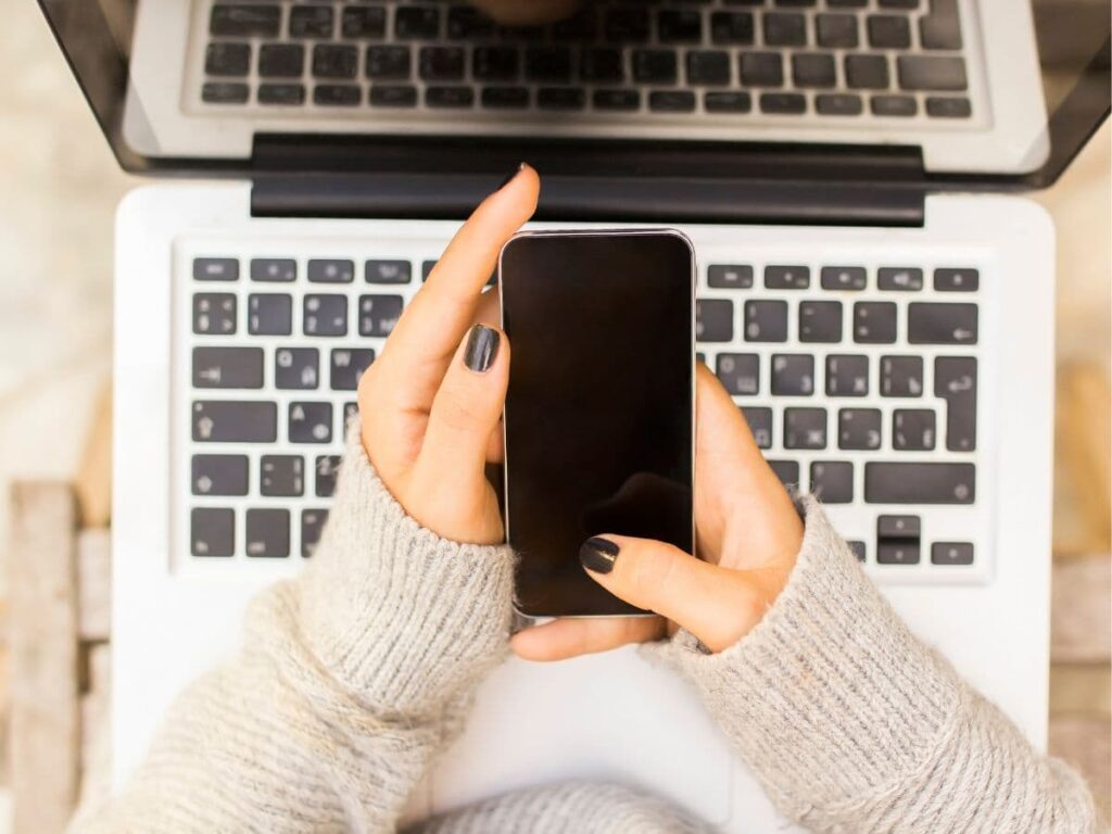 person with cell phone in hand and laptop on table 