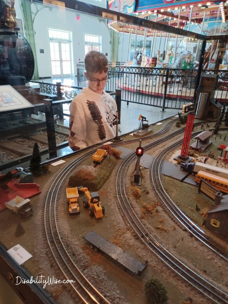 Teen boy looking at a toy train set at a museum working on skills in the  community 