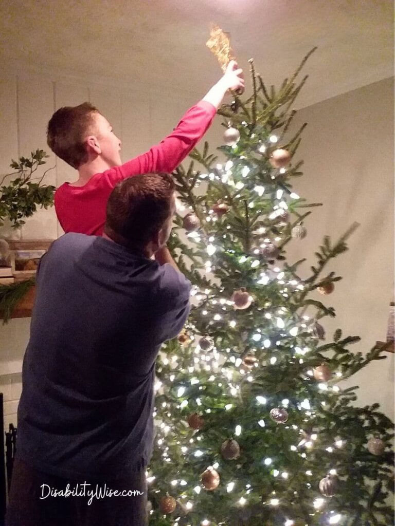 young boy with disabilities being lifted by father to put star on tree for the holidays