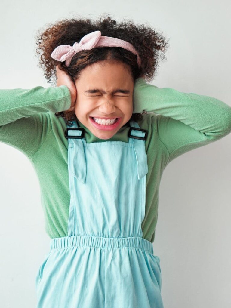 young girl holding her ears and making a grimacing face