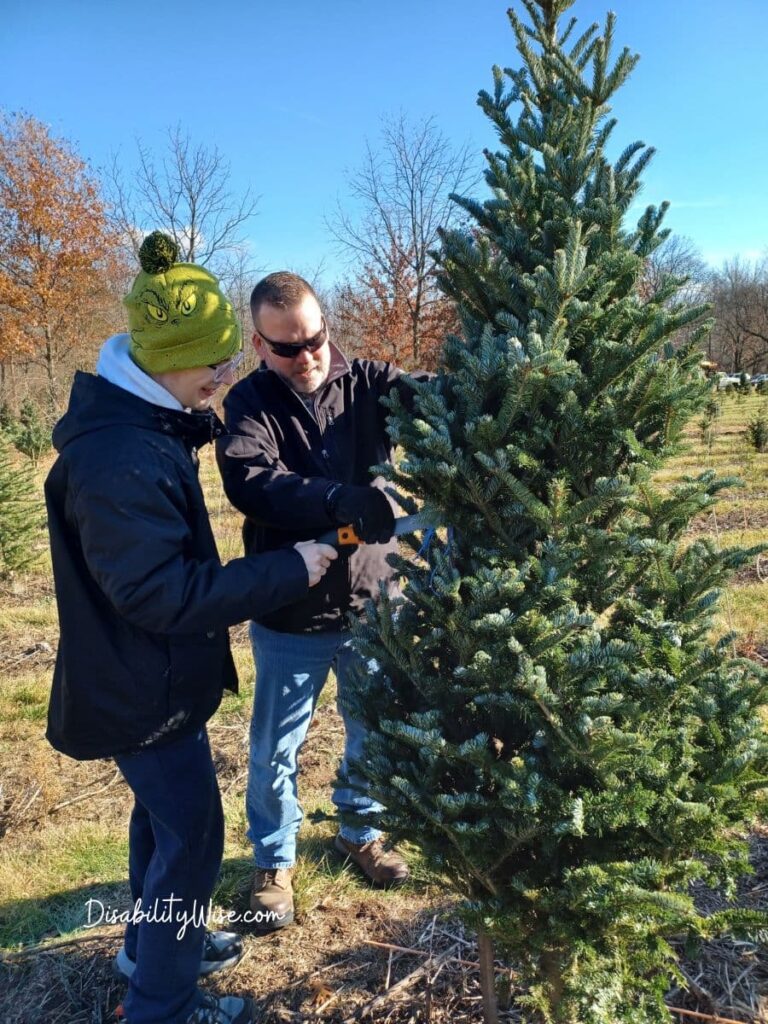 son with disability and father cutting a holiday tree 