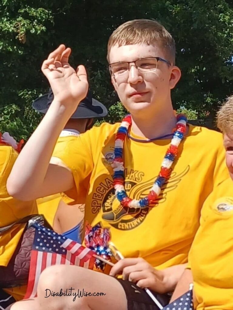 a teen boy with disabilities holding a small flag waving in a parade 