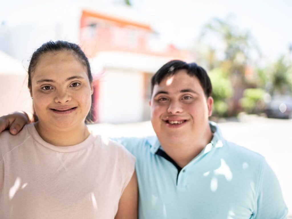 two adults with down syndrome standing in front of a house 