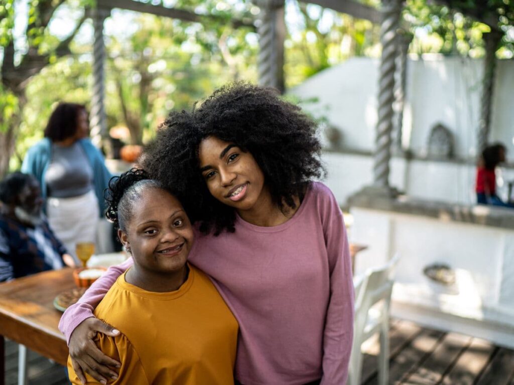 Two sisters of color standing next to each other. One has a developmental disability, the other does not.