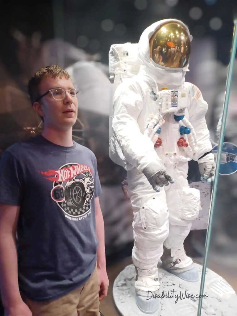 teen boy with developmental disabilities standing next to an astronaut statue 